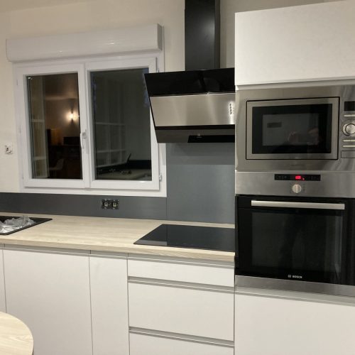 Détail du linéaire cuisson avec hotte noire et meubles sur mesure blancs à Urigny